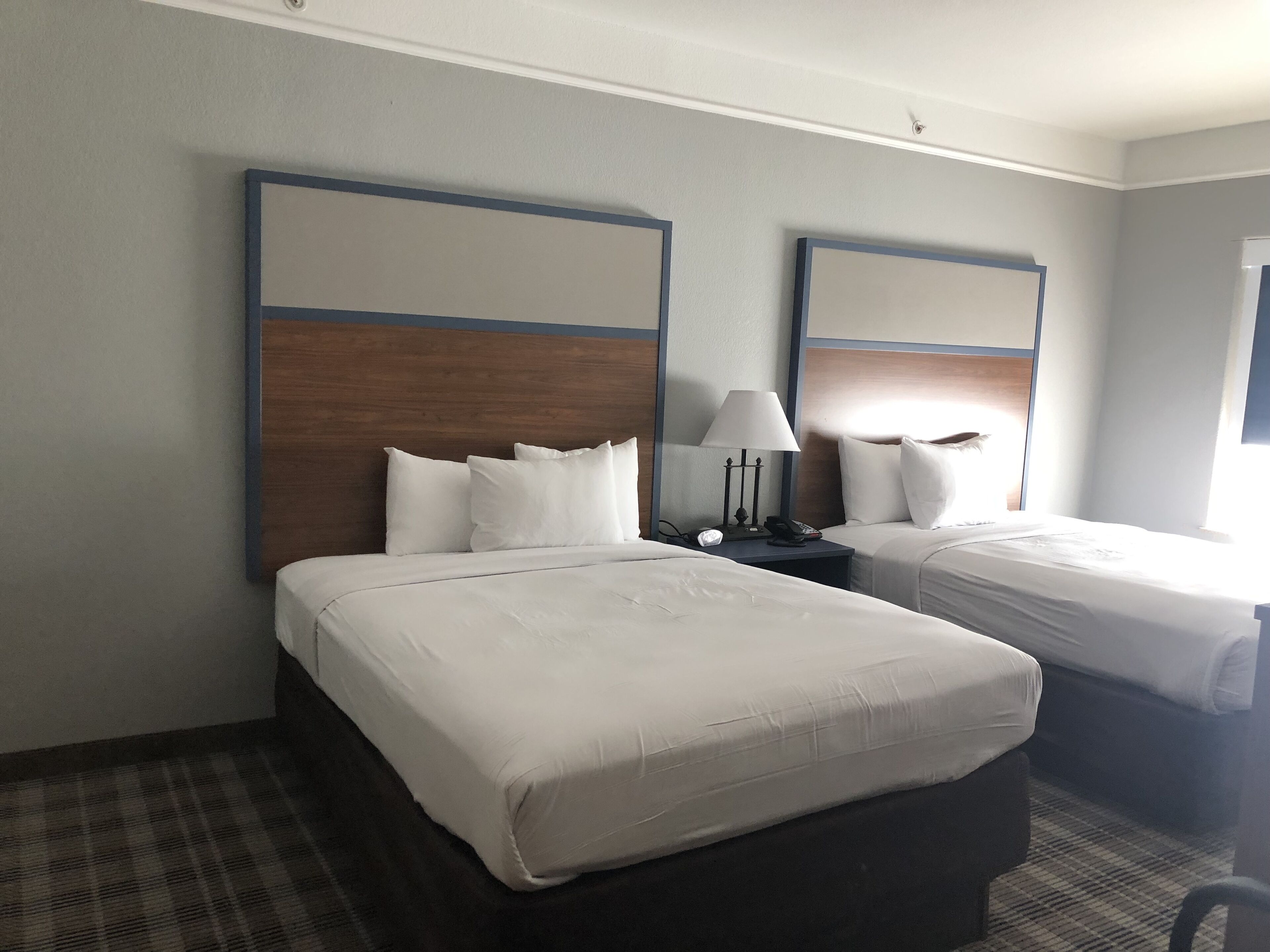 Ein Hotelzimmer mit zwei Betten, einem Nachttisch mit Lampe und einem Fenster.