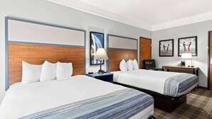 Een hotelkamer met twee bedden, een bureau, een stoel, een lamp en ingelijste foto's aan de muur.