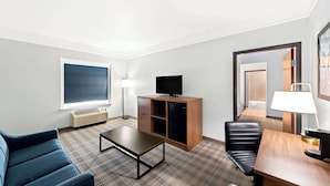 Een hotelkamer met een groot raam, een flatscreen televisie, een bureau met een lamp, een bank en een stoel.