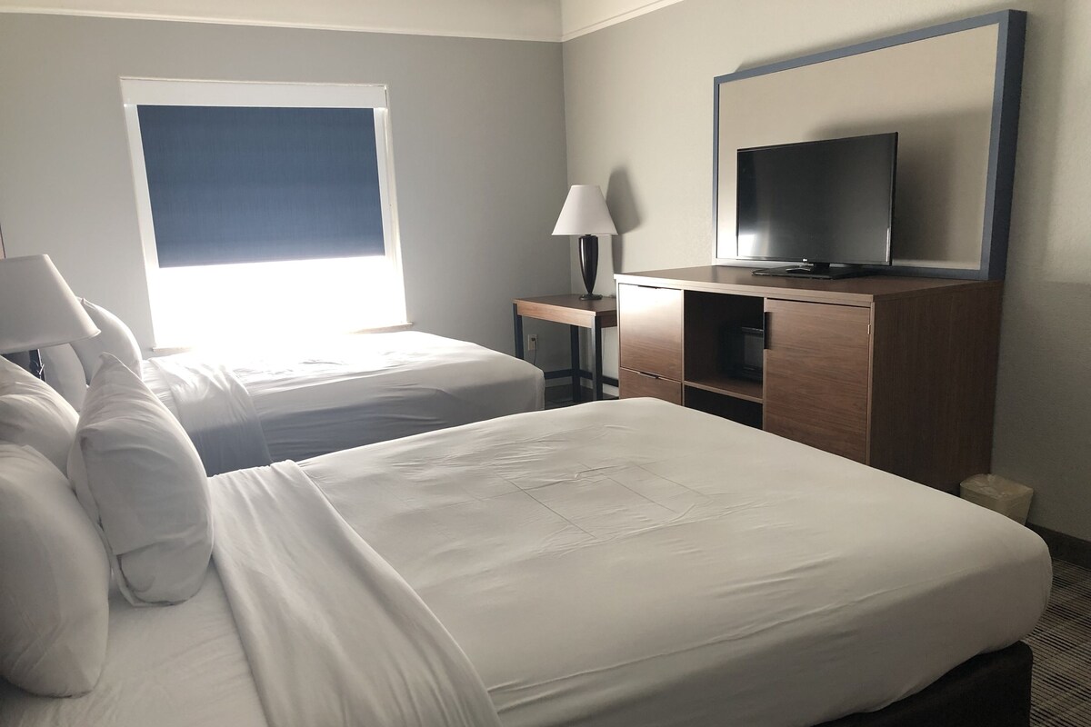 A hotel room with two beds, a TV, a desk, and a lamp.