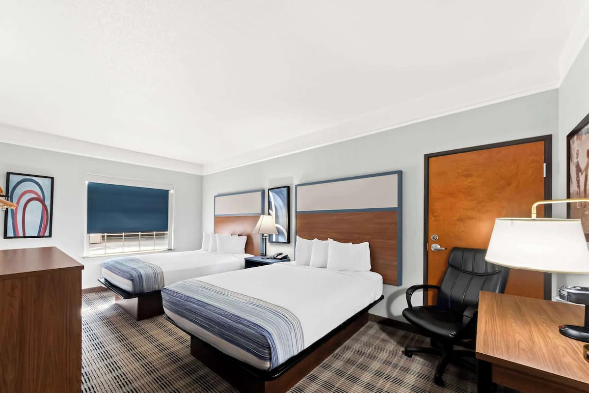 A hotel room with a large bed, a desk, a chair, and a window with blinds.