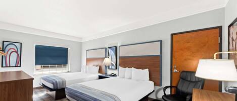 A hotel room with a large bed, a desk, a chair, and a window with blinds.