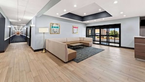 Een moderne lobby met een lange gang, een hoekbank, een vloerlamp en een groot raam met uitzicht.