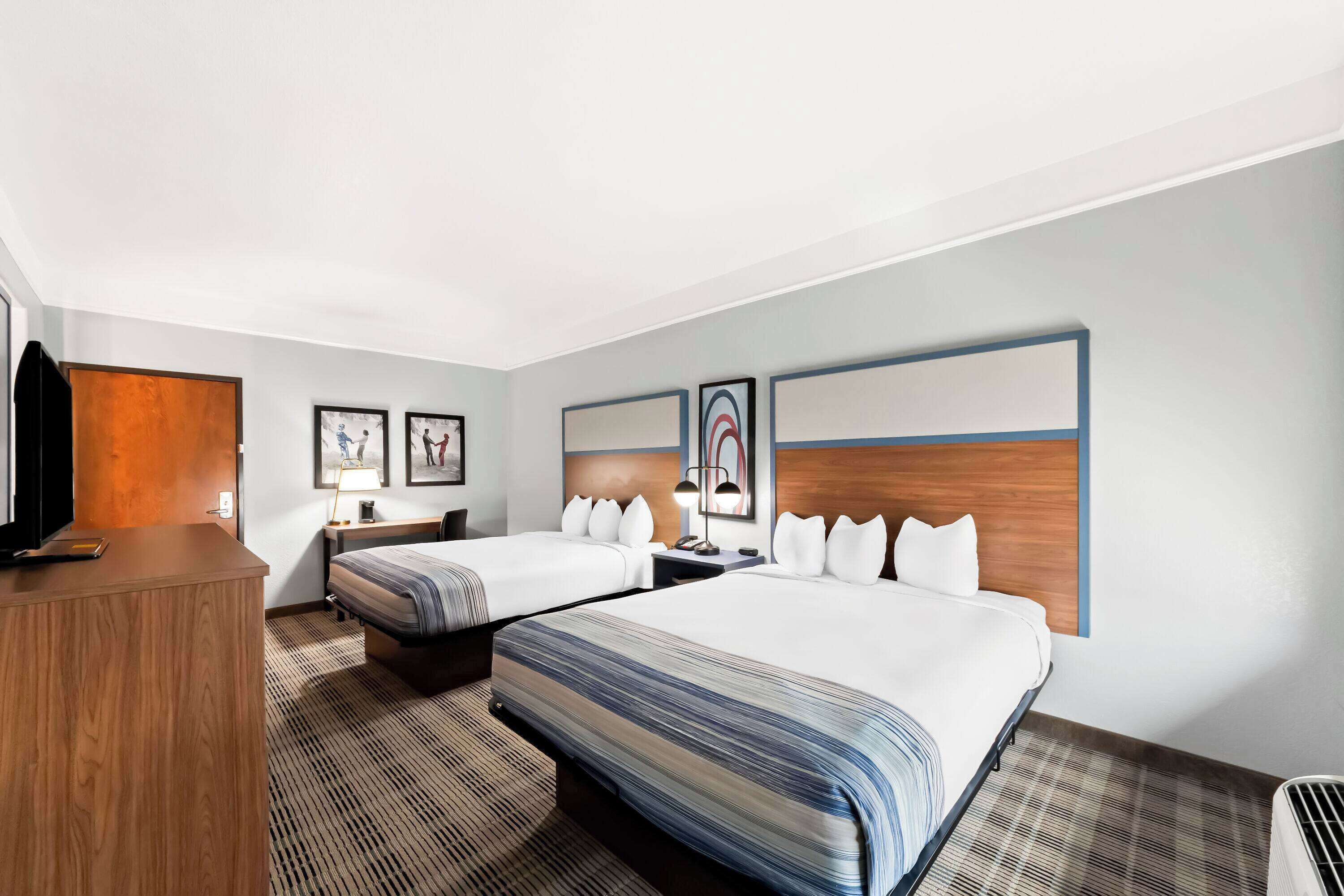 A hotel room with two beds, a wooden desk, a TV, and artwork on the walls.