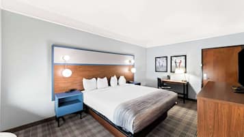 Una habitación de hotel con una cama grande, un escritorio, una silla, un armario y una mesita de noche.