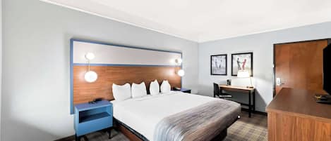 A hotel room with a large bed, a desk, a chair, a wardrobe, and a nightstand.