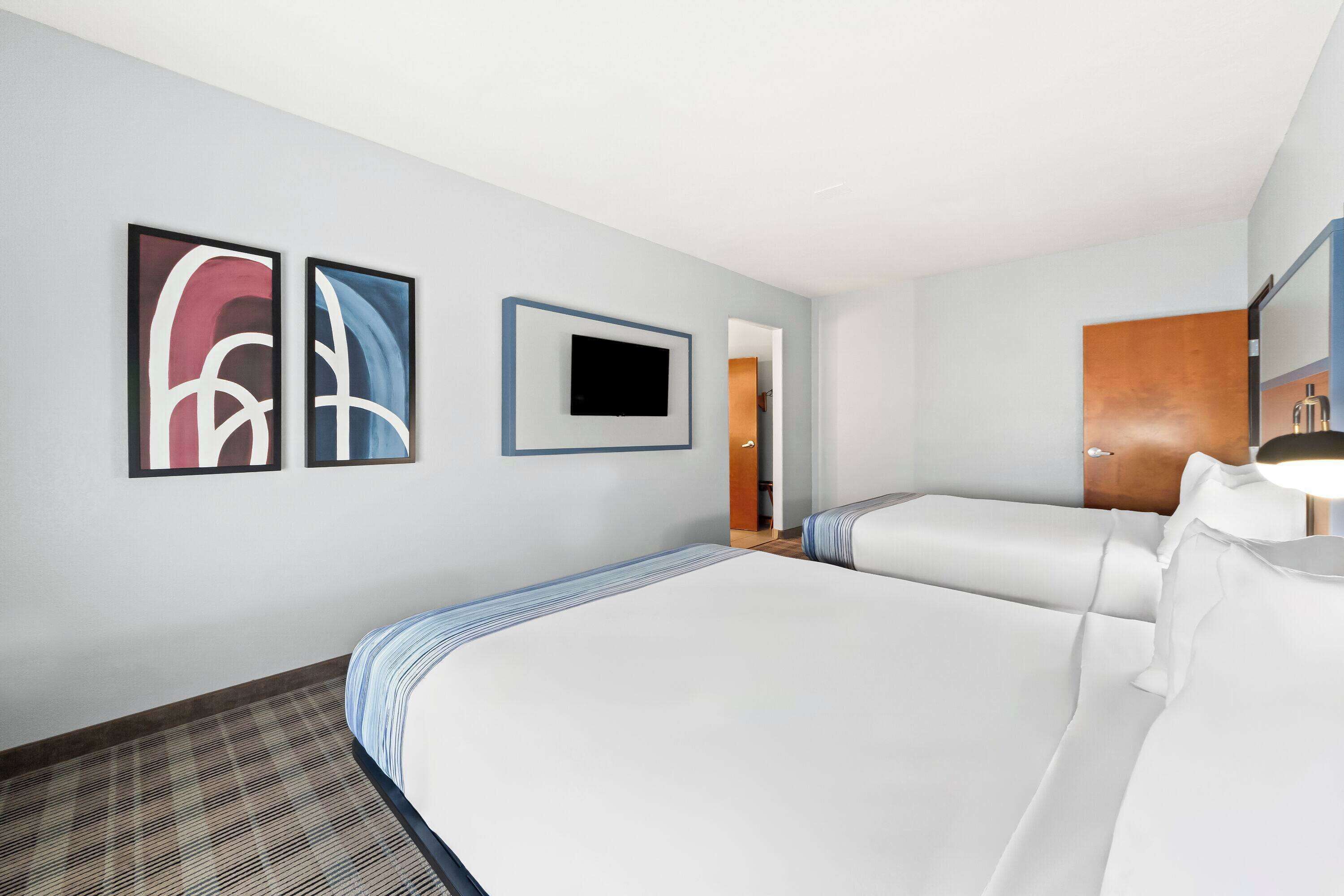 A hotel room with two beds, a flat-screen TV mounted on the wall, and abstract artwork on the wall.