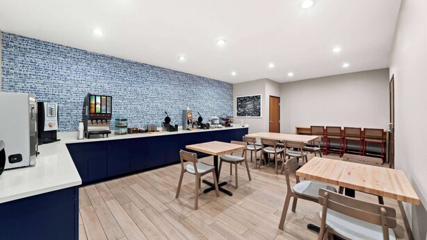 Een modern café met een blauwe betegelde muur, houten tafels en stoelen, en een koffiemachine.