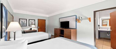 A hotel room with two beds, a television, a desk with a lamp, and a bathroom visible through an open door.