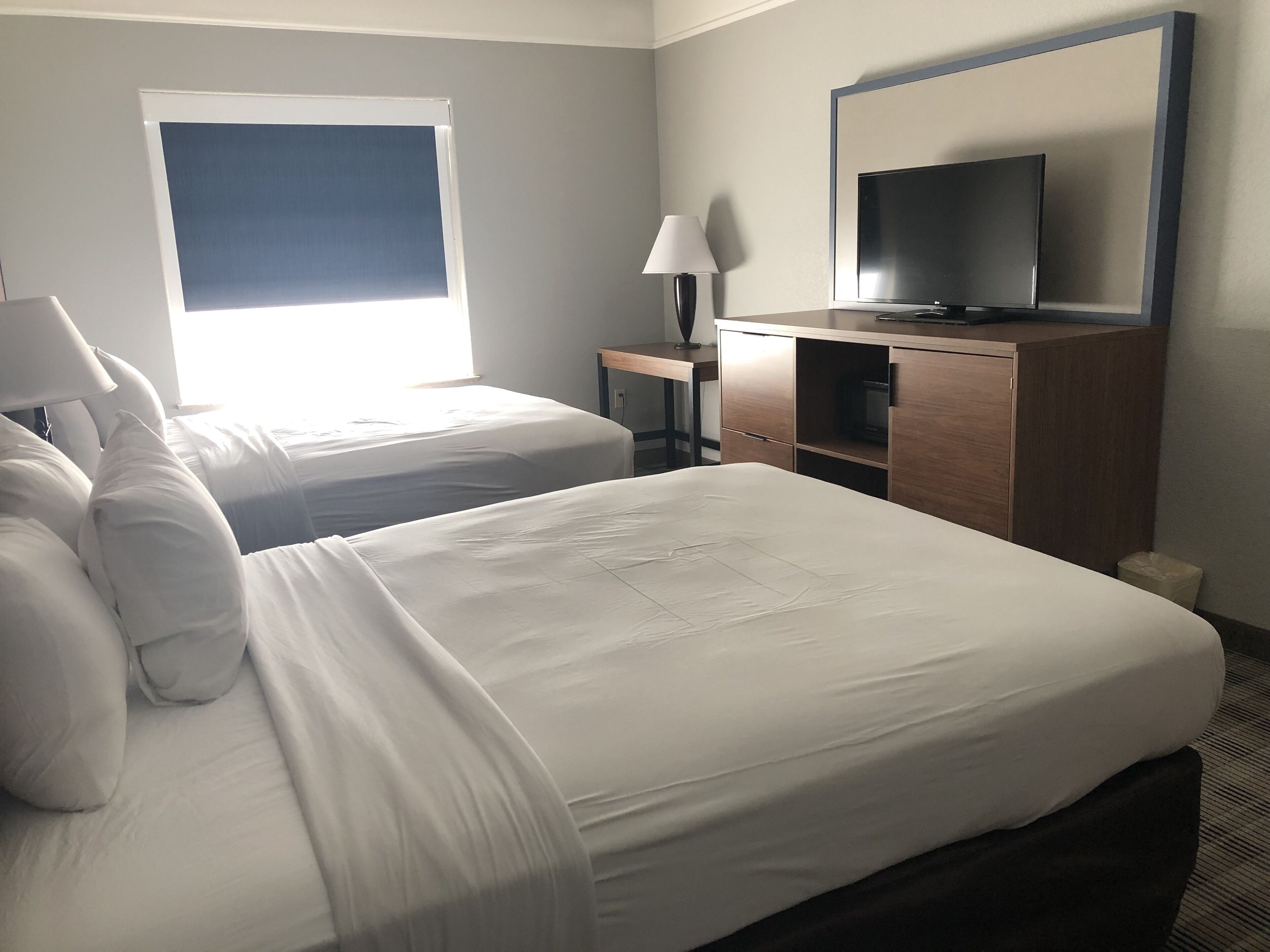 A hotel room with two beds, a TV, a desk, and a lamp.