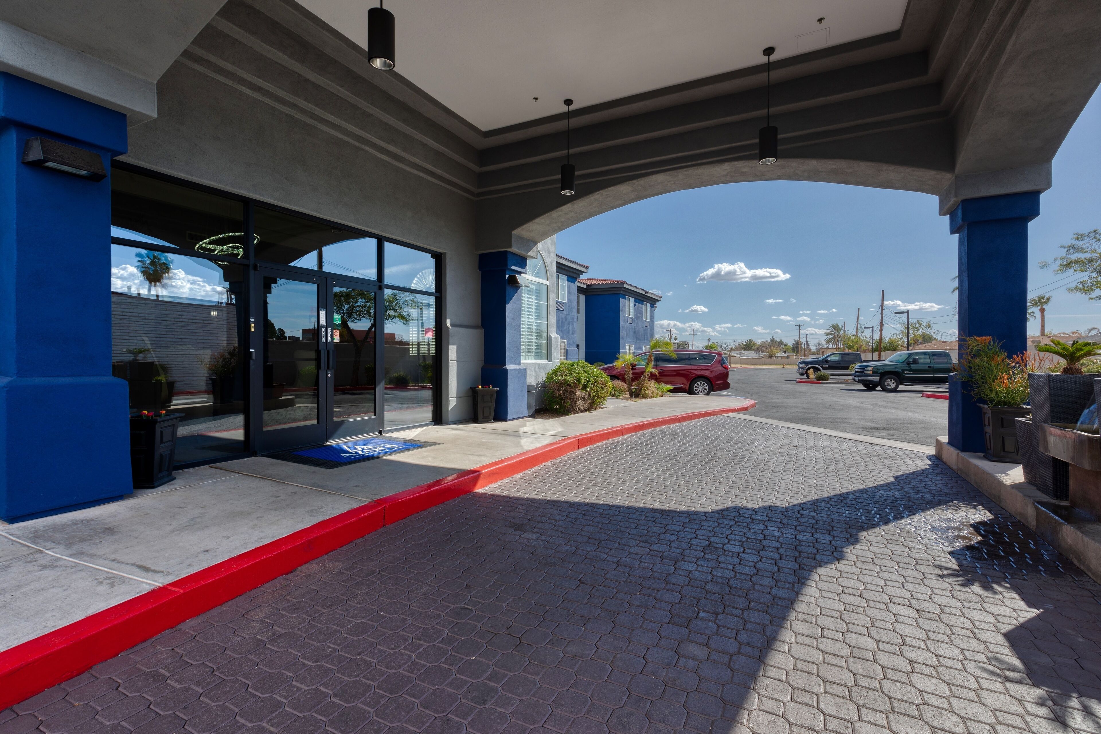 A hotel entrance with a covered walkway, glass doors, and a red curb.