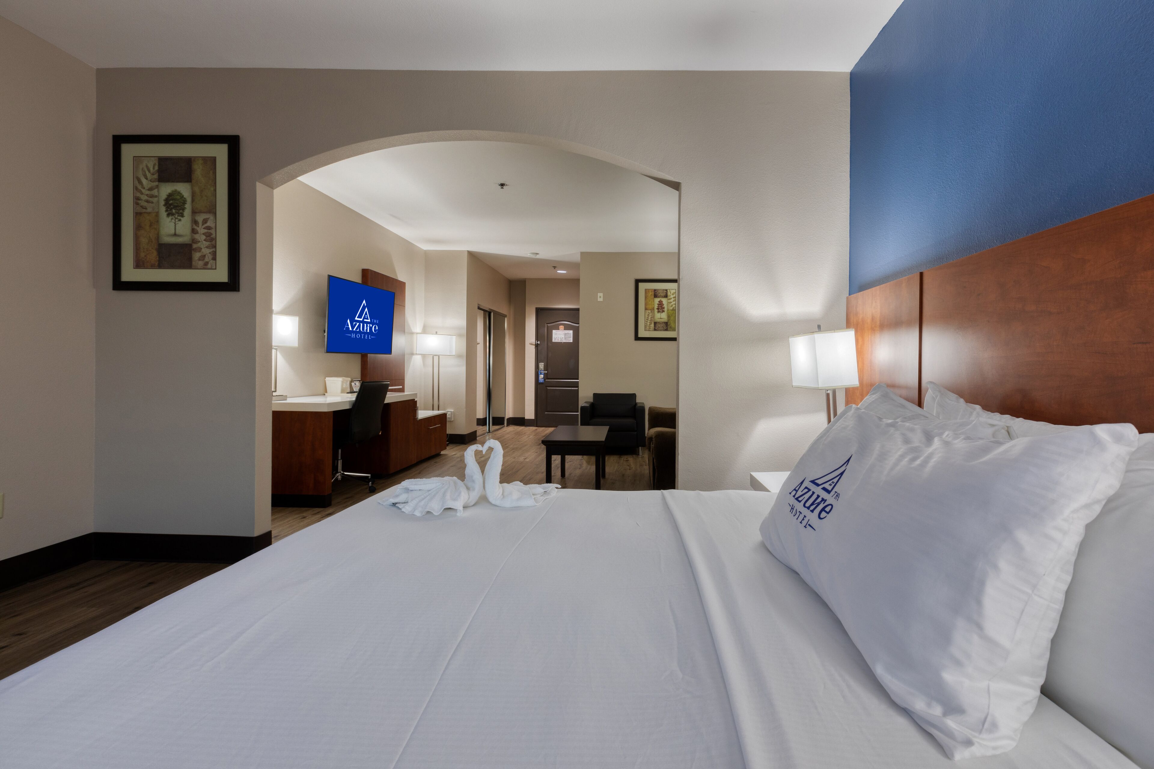 A hotel room with a large bed, a desk, a TV, and a view of the hallway.