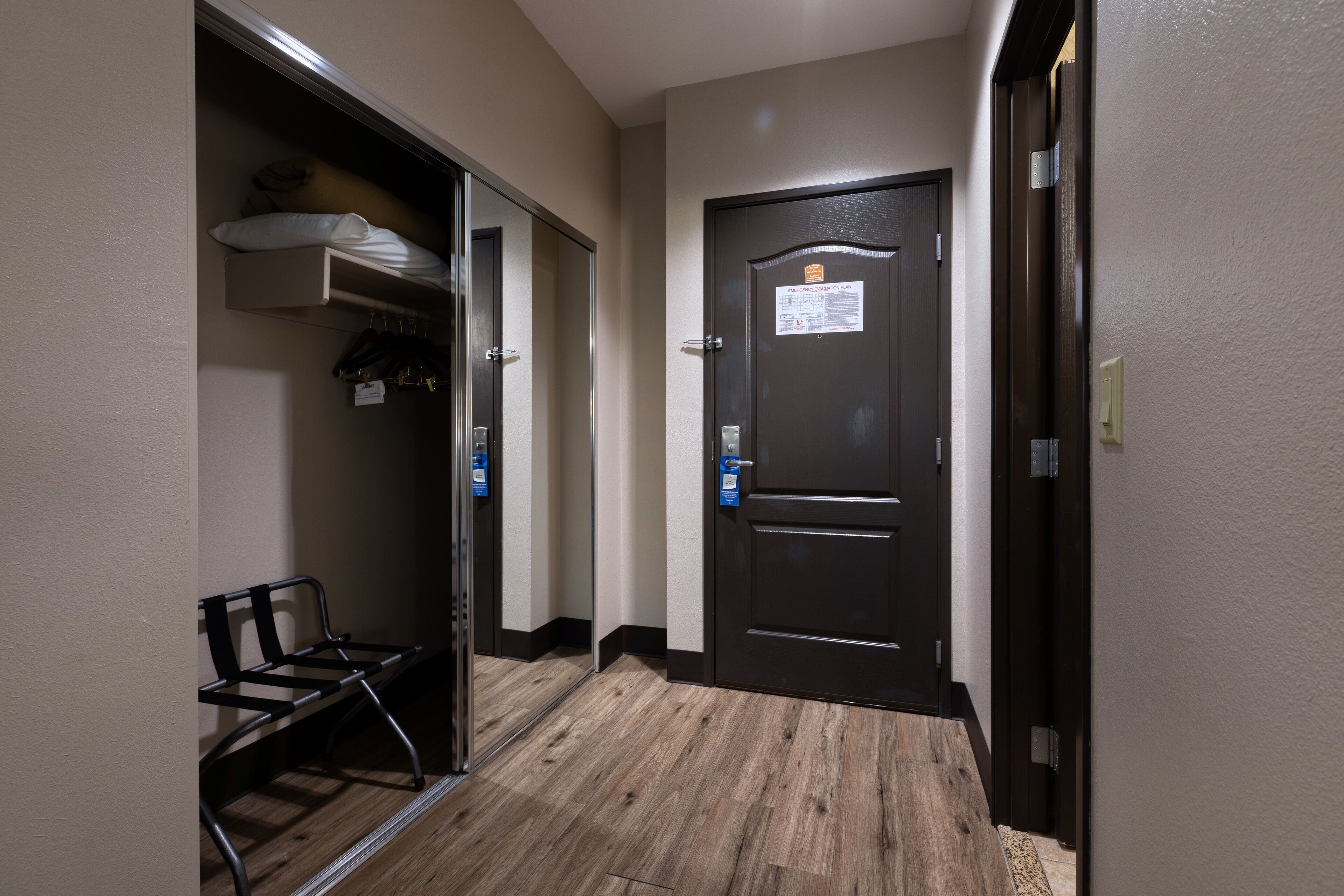 A hotel hallway with a bench, a coat closet, and a door with a sign.
