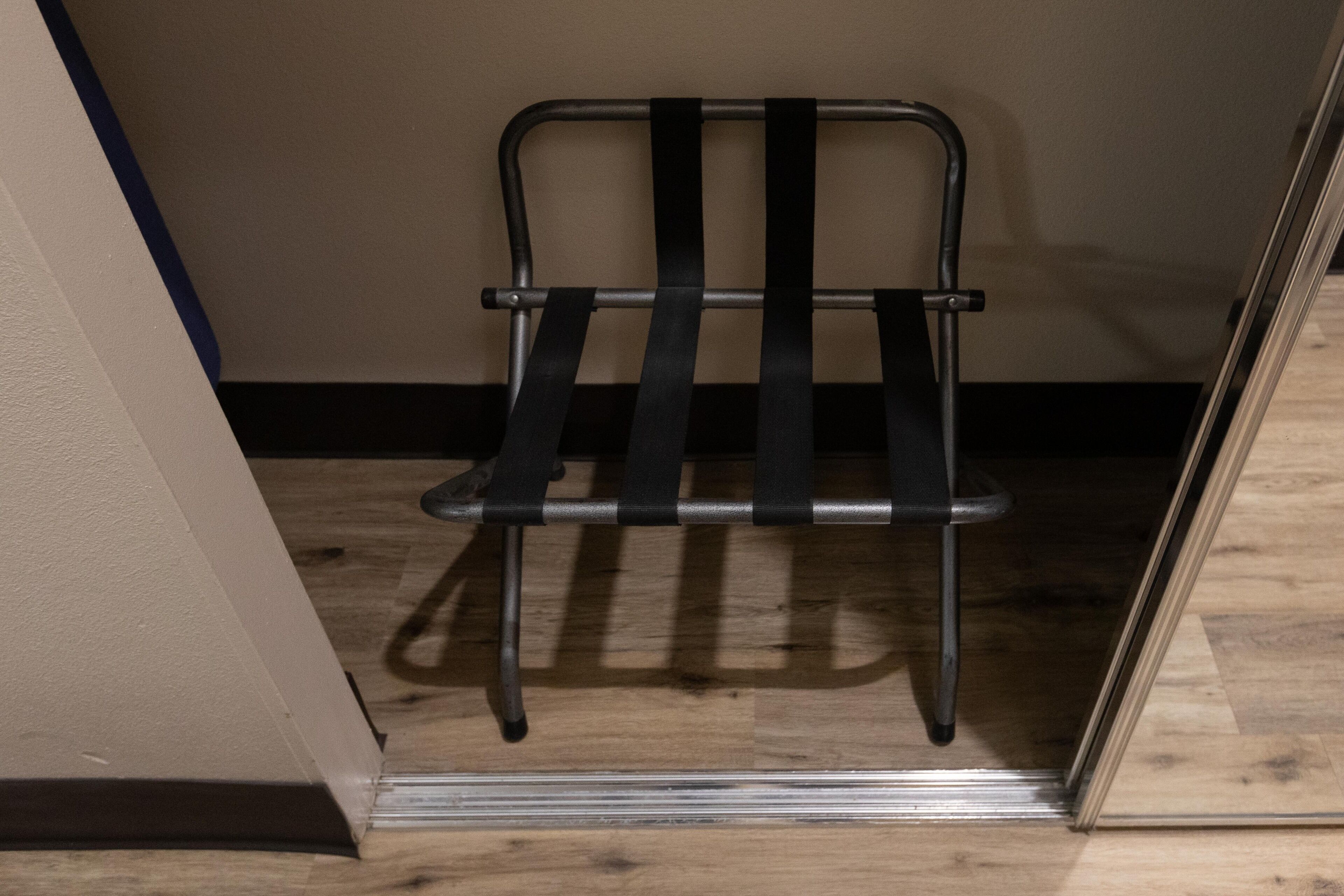 Une chaise en métal dotée d’un dossier et d’une assise à lattes, placée dans une pièce au plancher en bois et aux murs unis.