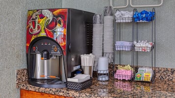 Una máquina de café con un diseño llamativo, vasos de papel apilados y distintos productos de papel sobre una encimera.