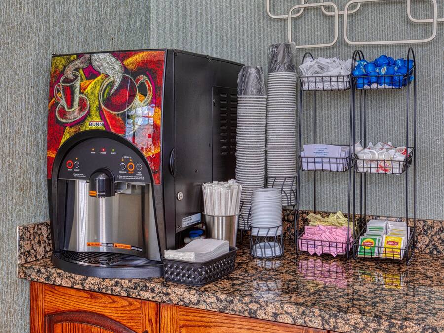 Eine Kaffeemaschine mit farbigem Design, gestapelte Papierbecher und diverse Papierprodukte auf einer Theke.