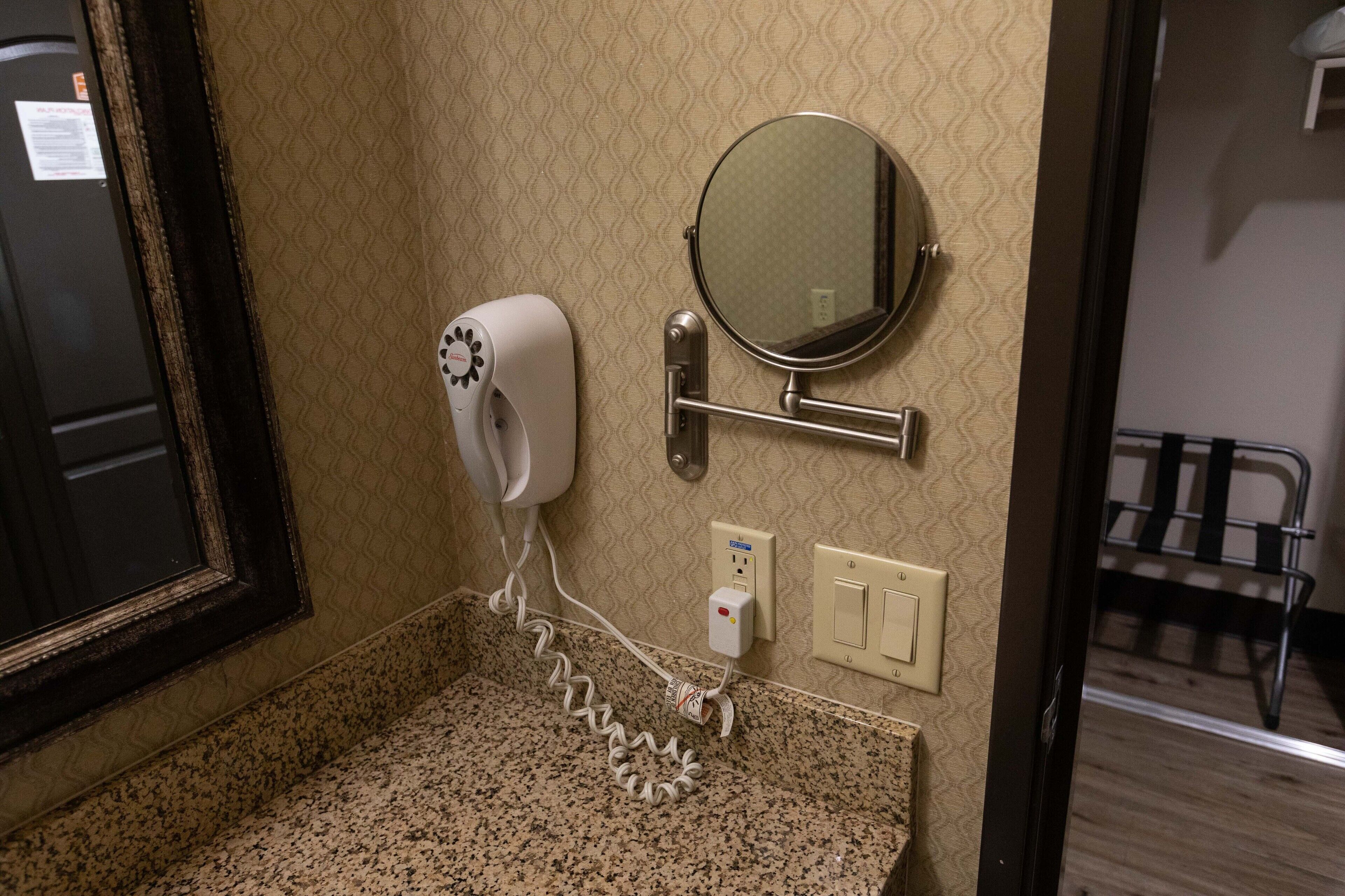 Un baño con secador de pelo, un espejo redondo y un perchero para toallas.