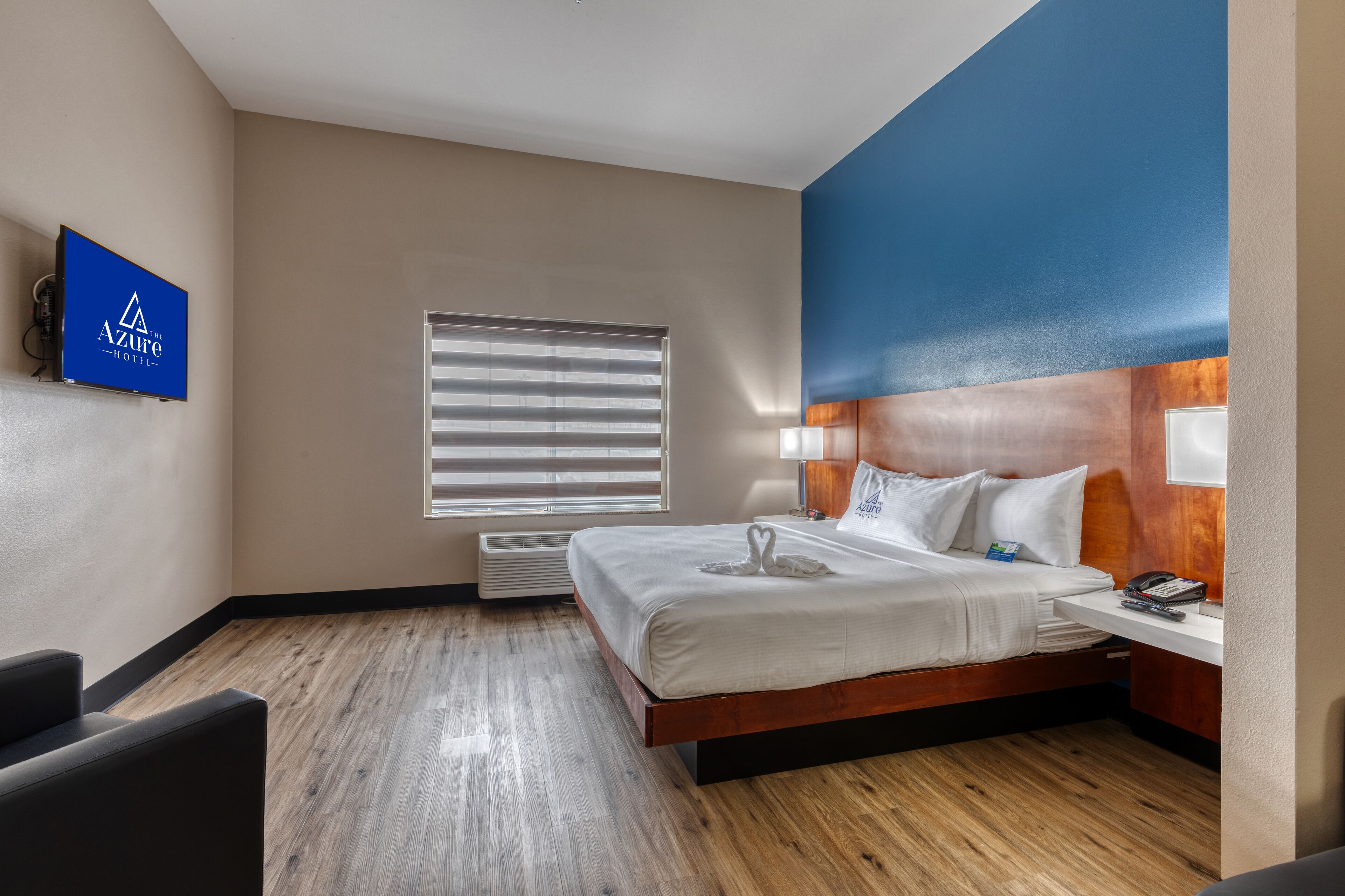 A hotel room with a bed, bedside table, lamp, and a television mounted on the wall.