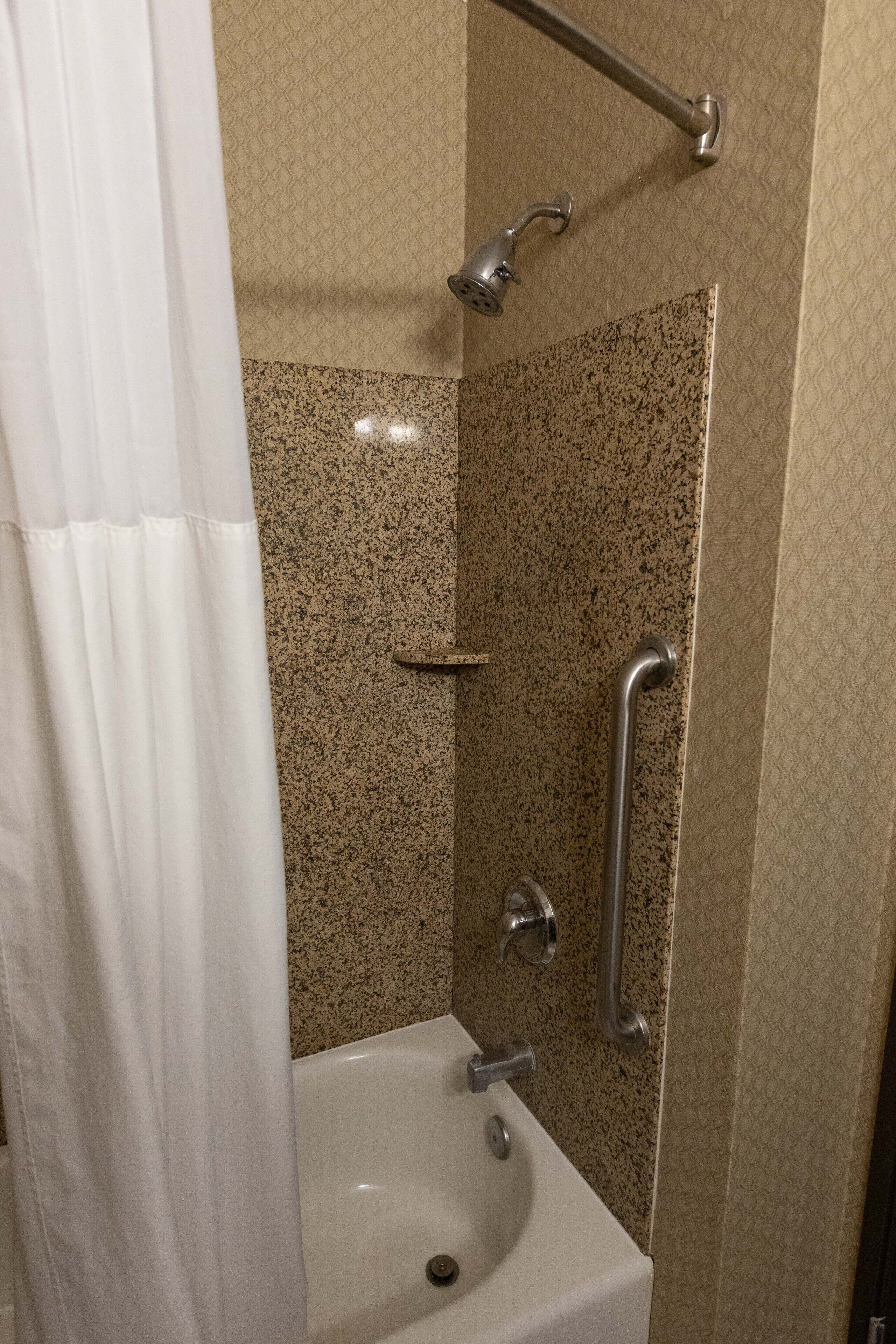 Een badkamer met douche, handgrepen en wastafel.