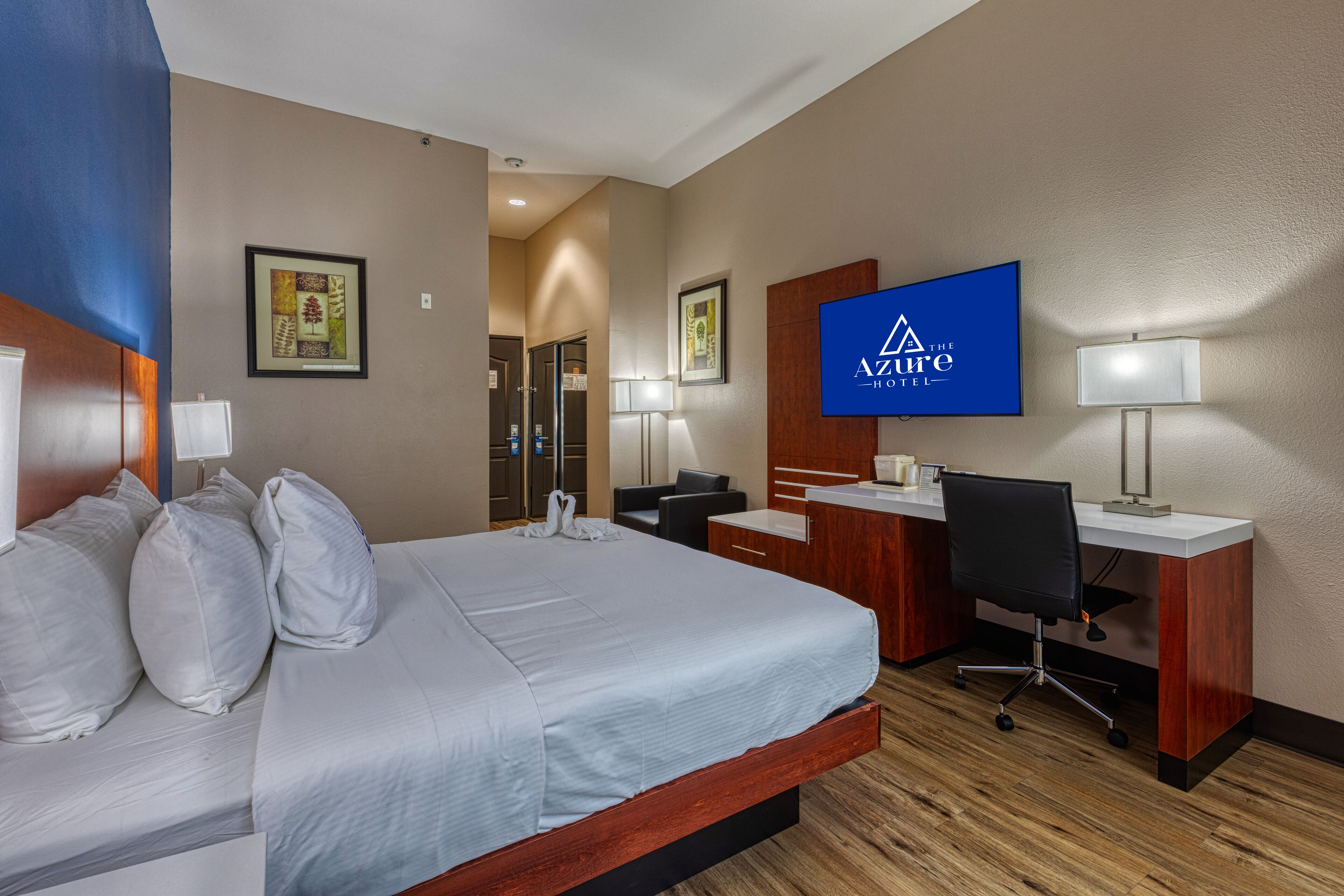 A hotel room with a bed, desk, chair, and a television displaying the hotel name.