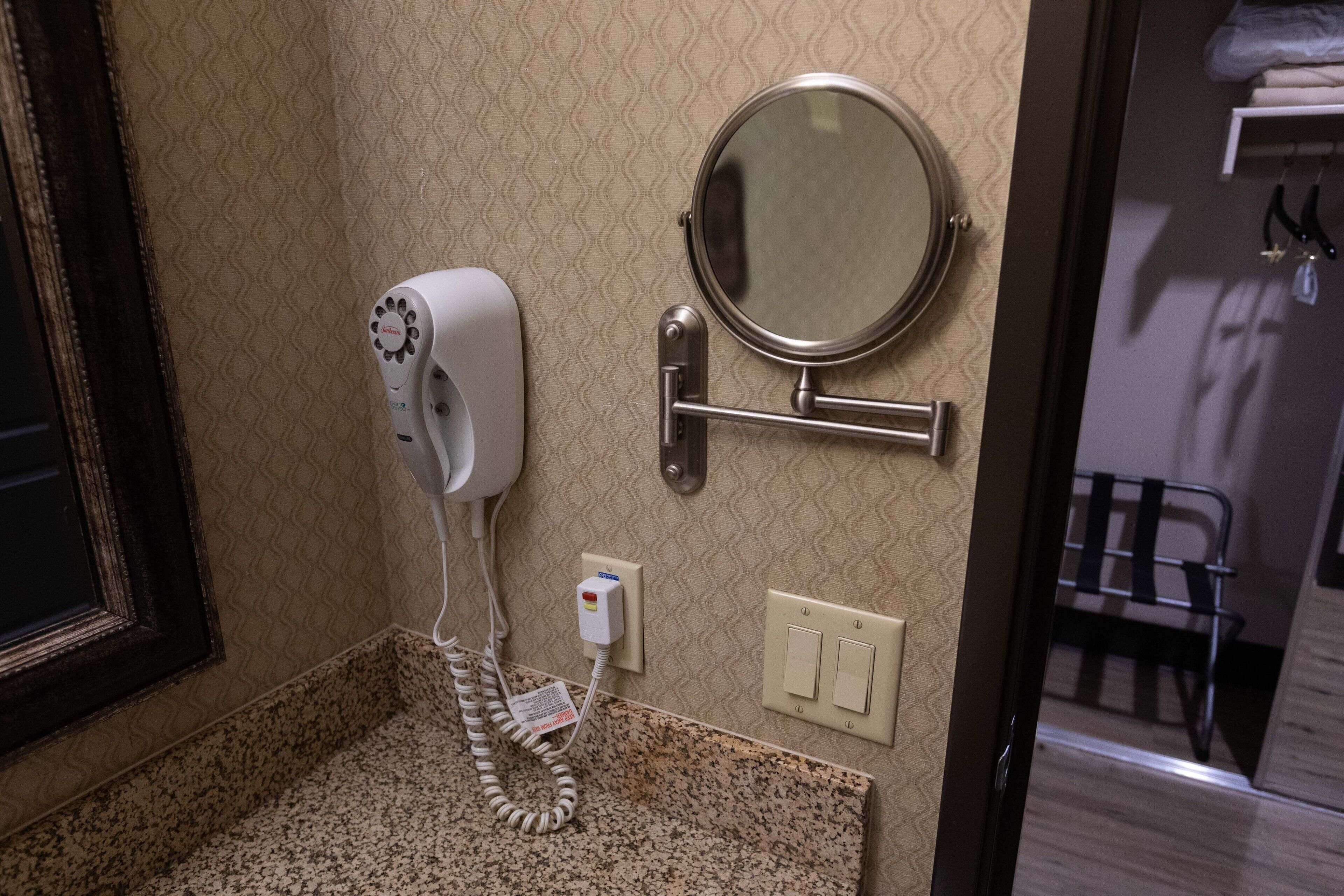 A bathroom with a hairdryer, a round mirror, and a towel rack.