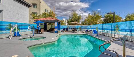 Una piscina con valla azul, sillas de descanso y una zona de estar cubierta.