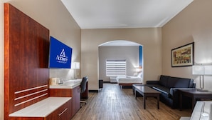 Habitación de hotel con armario de madera, escritorio con silla, cama, sofá y televisor montado en la pared.
