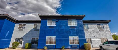 A modern building with a blue facade, multiple windows, and a parking lot.