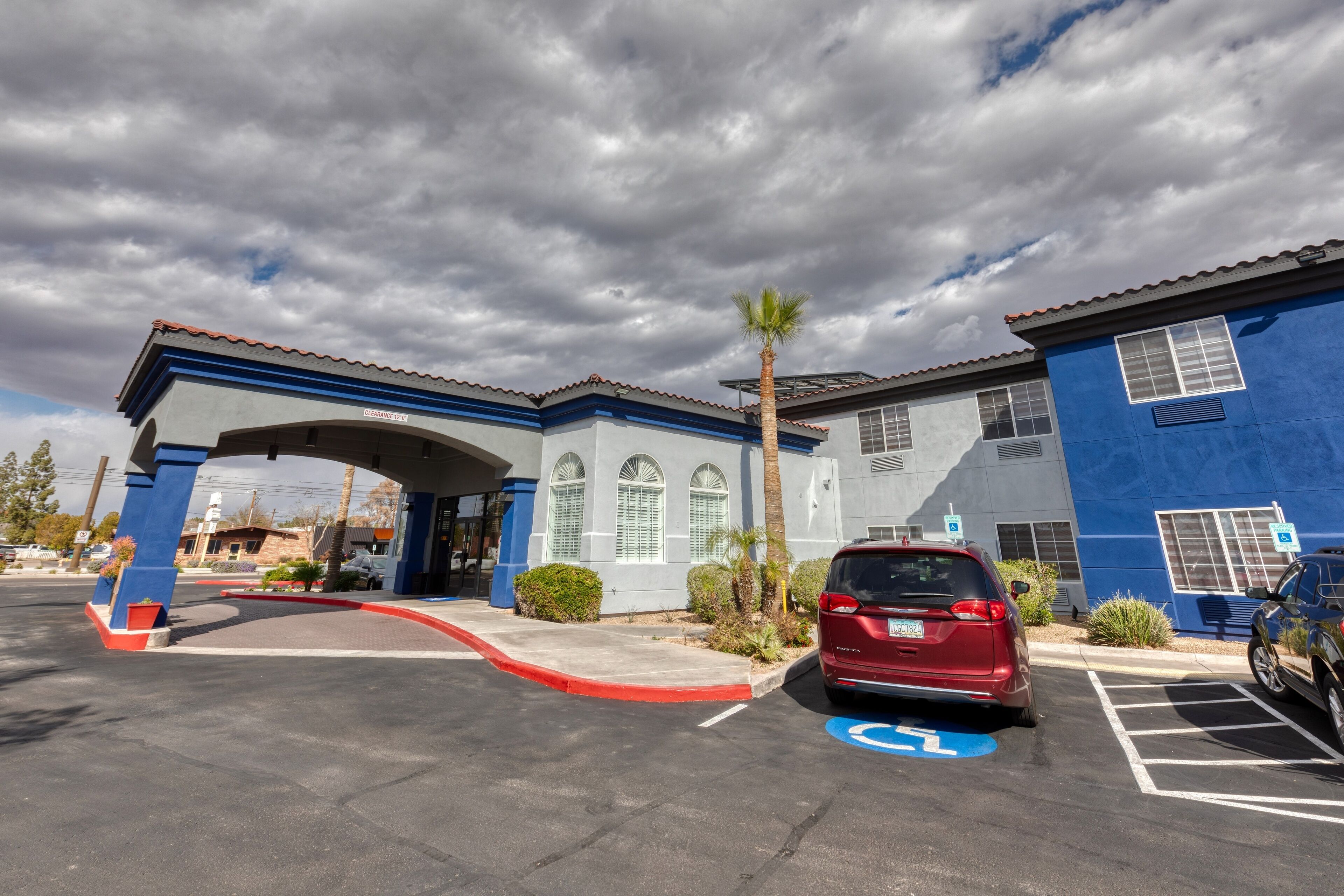 A parking lot with a red car and a blue building with a covered entrance.