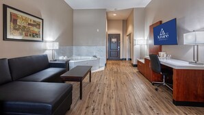 Una habitación de hotel con sofá, escritorio, silla, bañera y una obra de arte enmarcada en la pared.