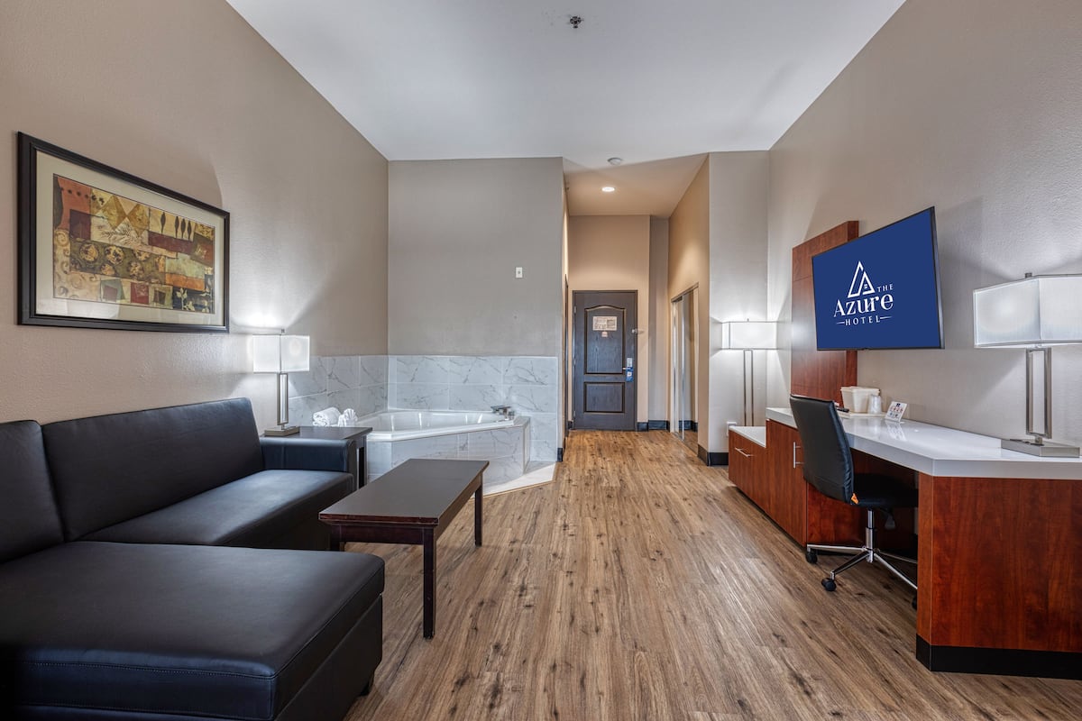 Une chambre d’hôtel équipée d’un canapé, d’un bureau, d’une chaise, d’une baignoire et d’une œuvre d’art encadrée au mur.