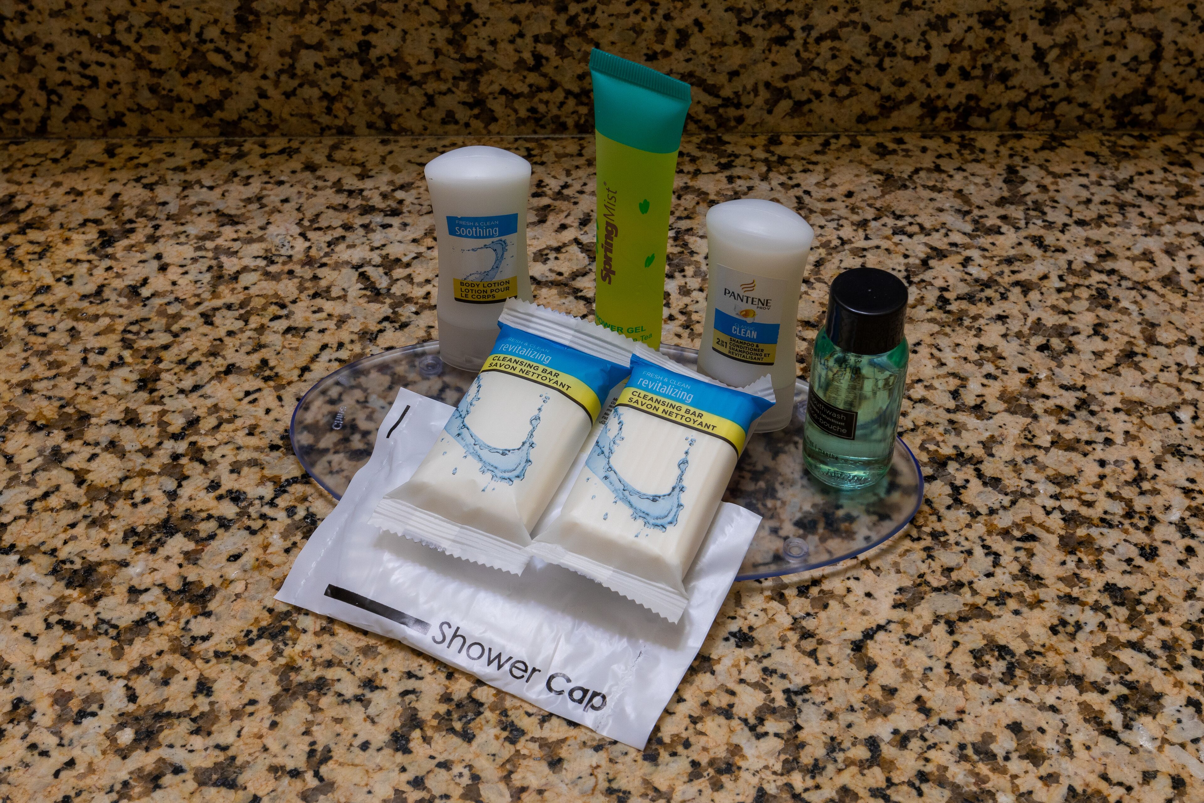 A granite countertop with various toiletries including a shower cap, body lotion, and cleaning products.