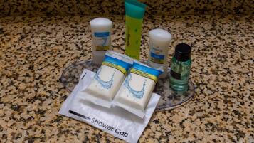 A granite countertop with various toiletries including a shower cap, body lotion, and cleaning products.