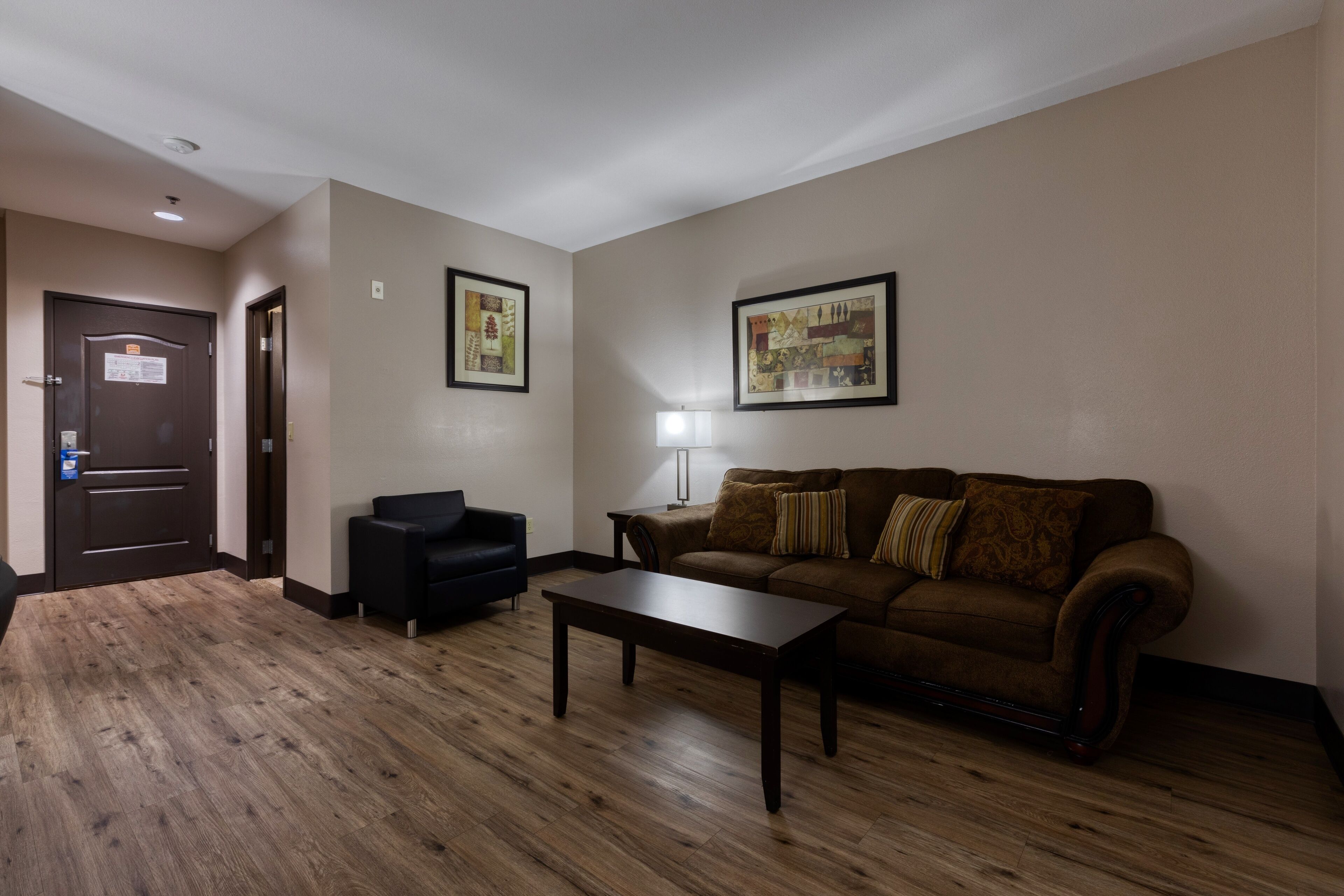 Ein Wohnzimmer mit einem braunen Sofa, einem schwarzen Sessel, einem Holztisch und zwei gerahmten Bildern an der Wand.