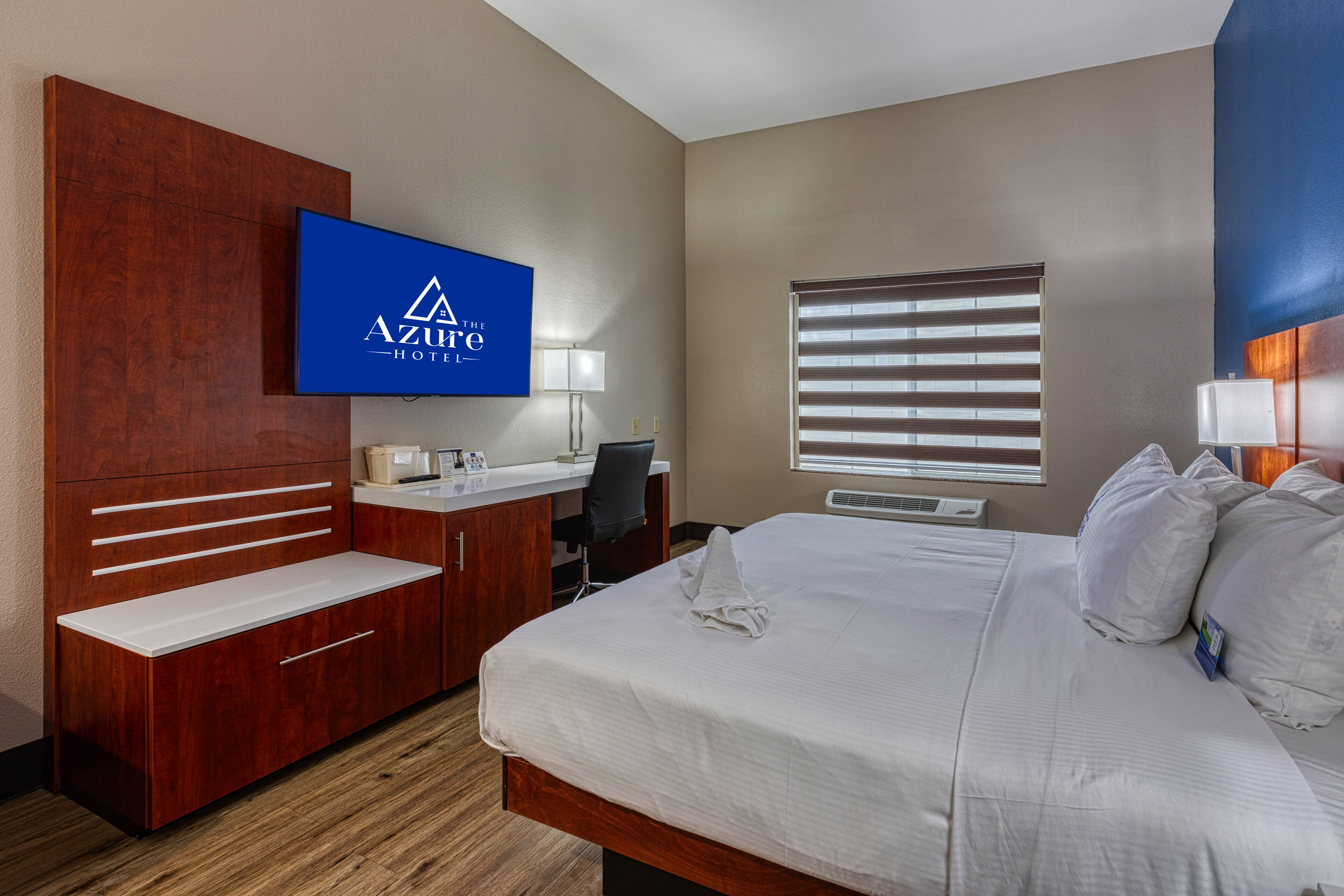 Een hotelkamer met een bed, bureau, televisie en een raam met jaloezieën.