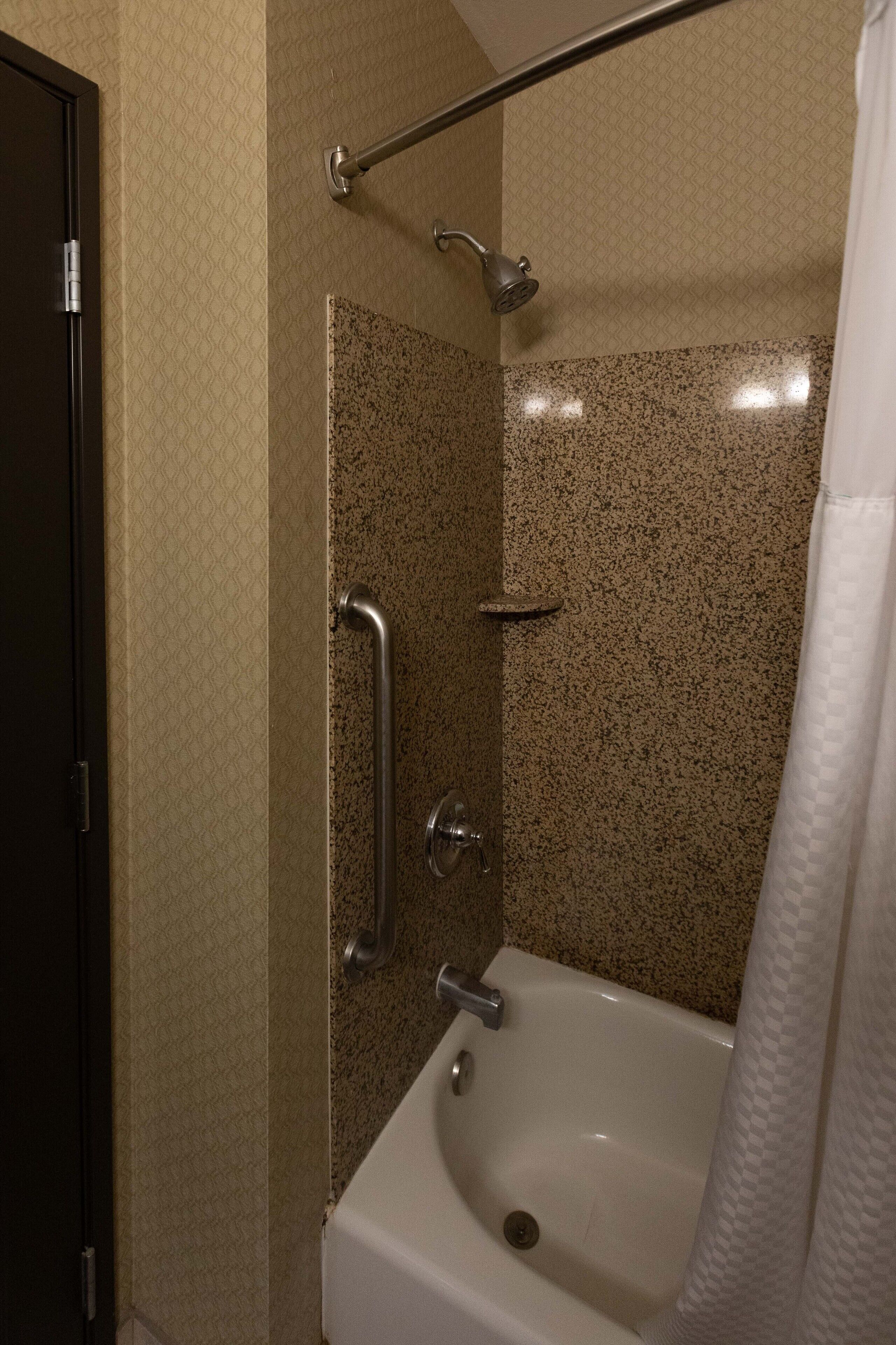 Un baño con bañera, ducha con barra de apoyo y una puerta.