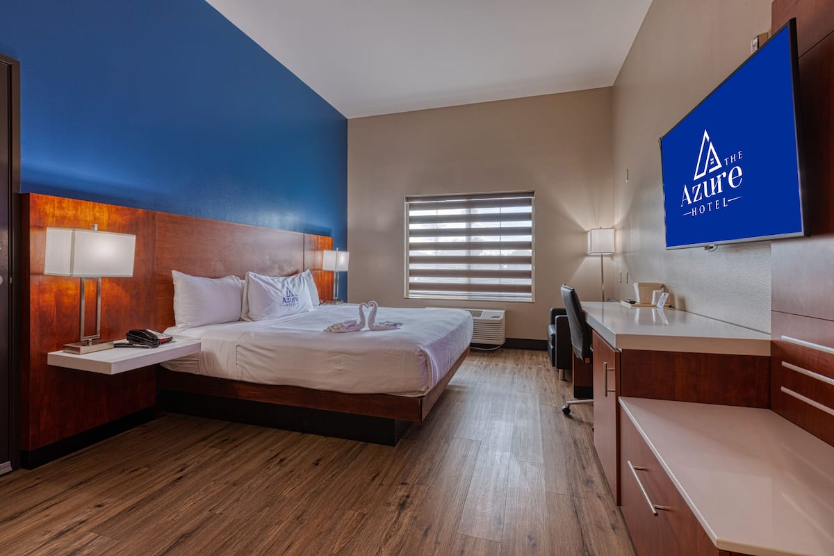 Une chambre d’hôtel comprenant un lit, des tables de chevet, un bureau, une télévision et une fenêtre avec des stores.