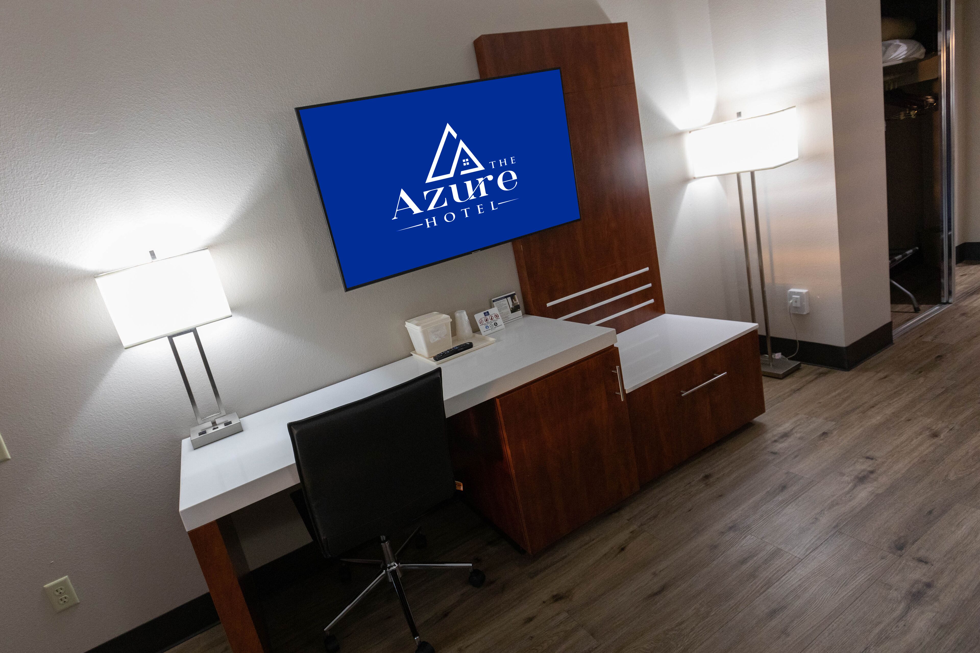 A hotel room with a desk, chair, and a TV mounted on the wall displaying the Azure Hotel logo.