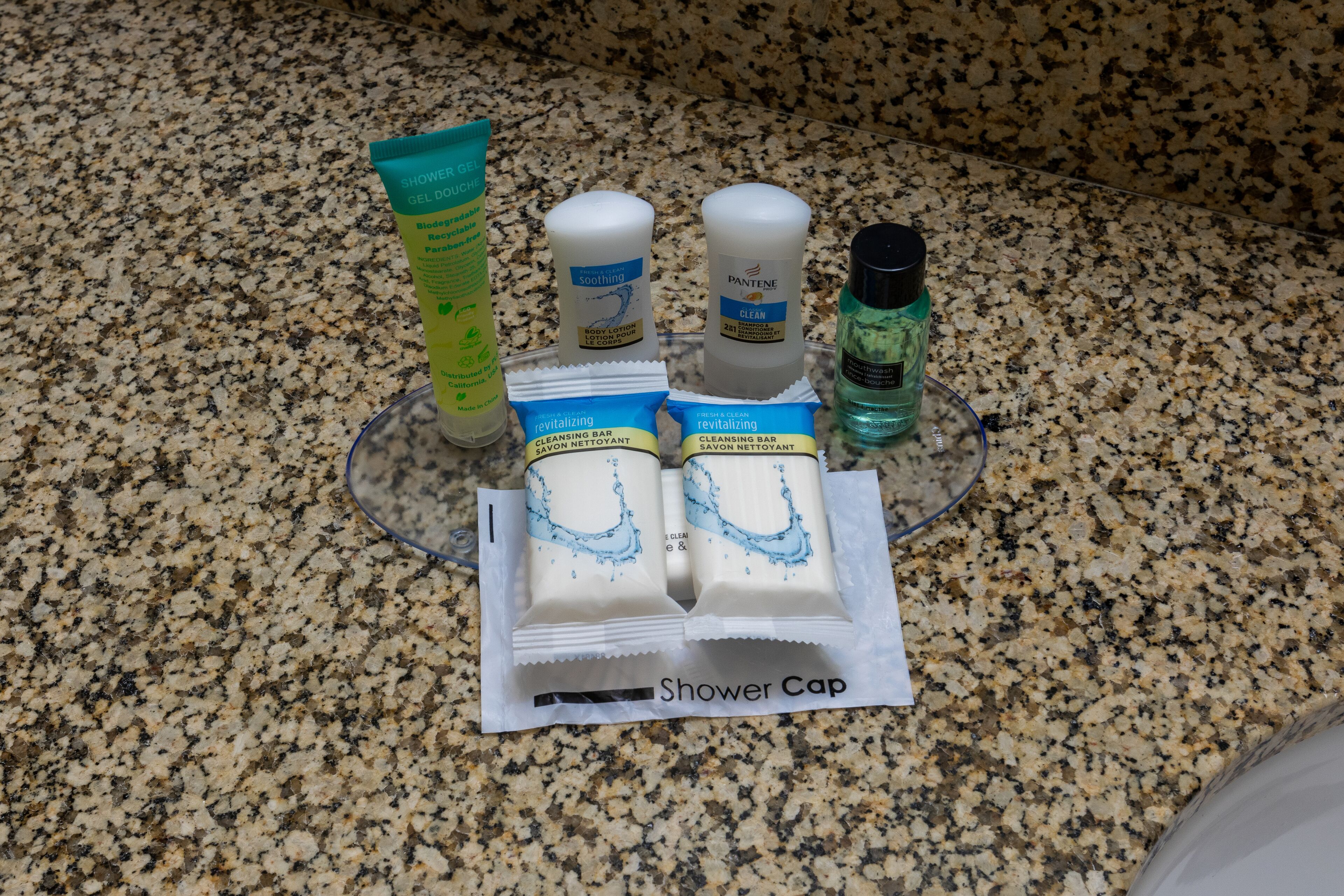 A set of toiletries on a granite countertop, including a shower cap, body lotion, and cleansing bar.