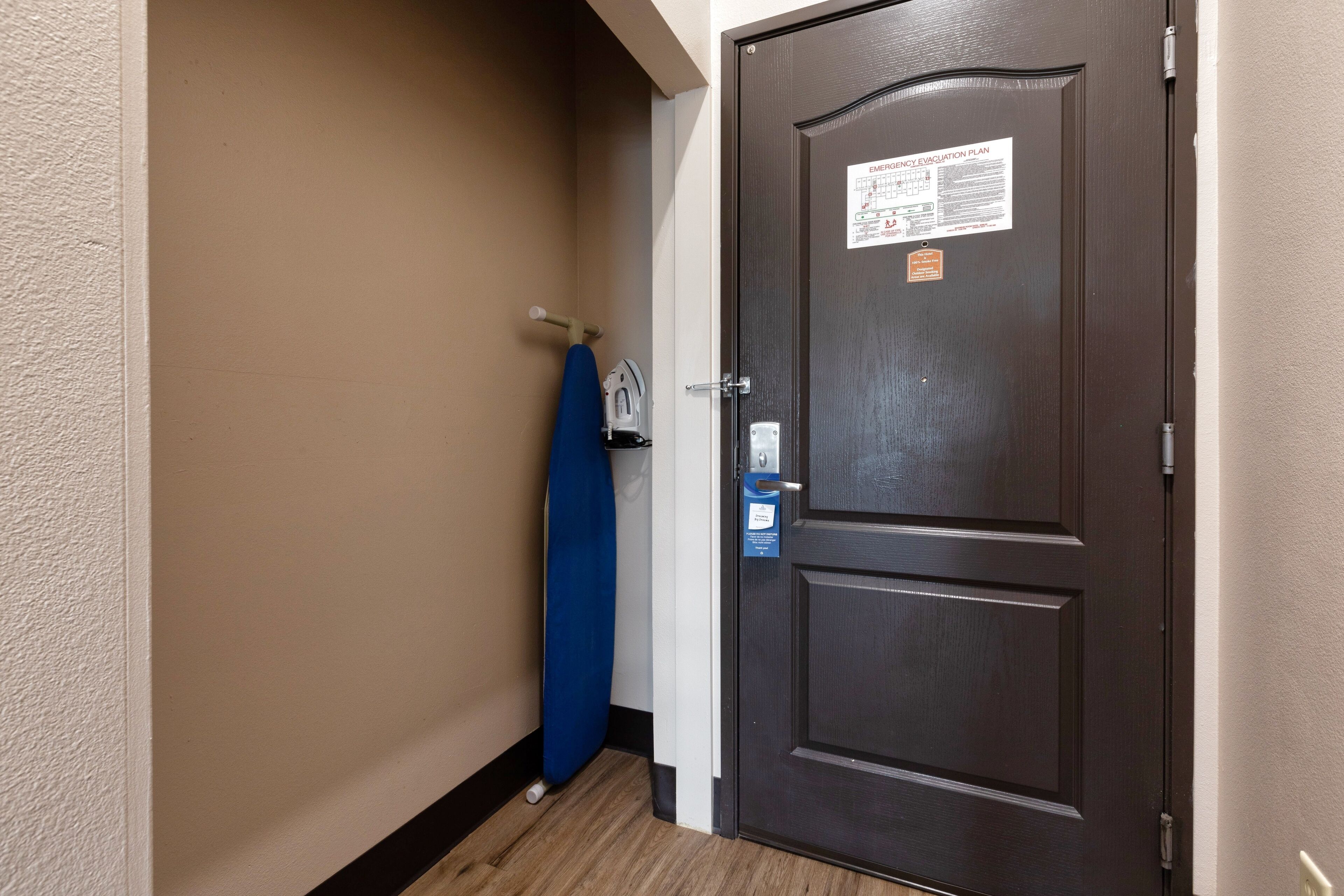 Uma porta de madeira escura com uma placa de plano de evacuação de emergência, uma toalha azul pendurada em um gancho e uma parede branca com acabamento texturizado.