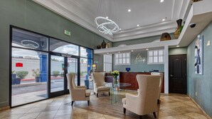 A hotel lobby with a reception desk, seating area, and large glass doors leading outside.