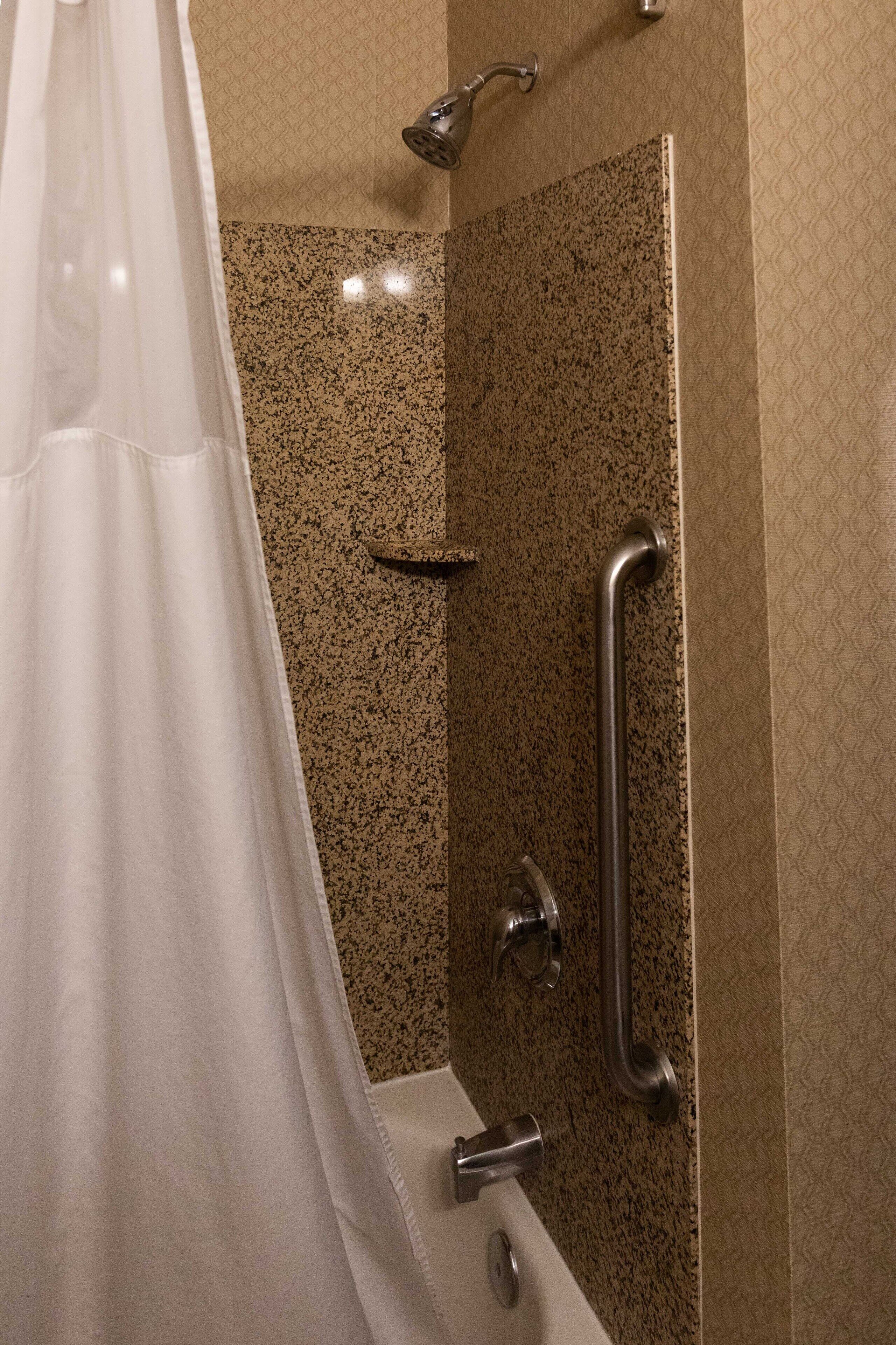 Ein Badezimmer mit Dusche, Haltegriffen und einer Badewanne.