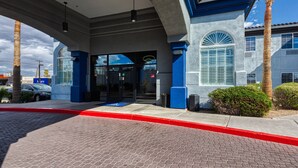 A hotel entrance with a red curb, palm trees, and a clear blue sky.