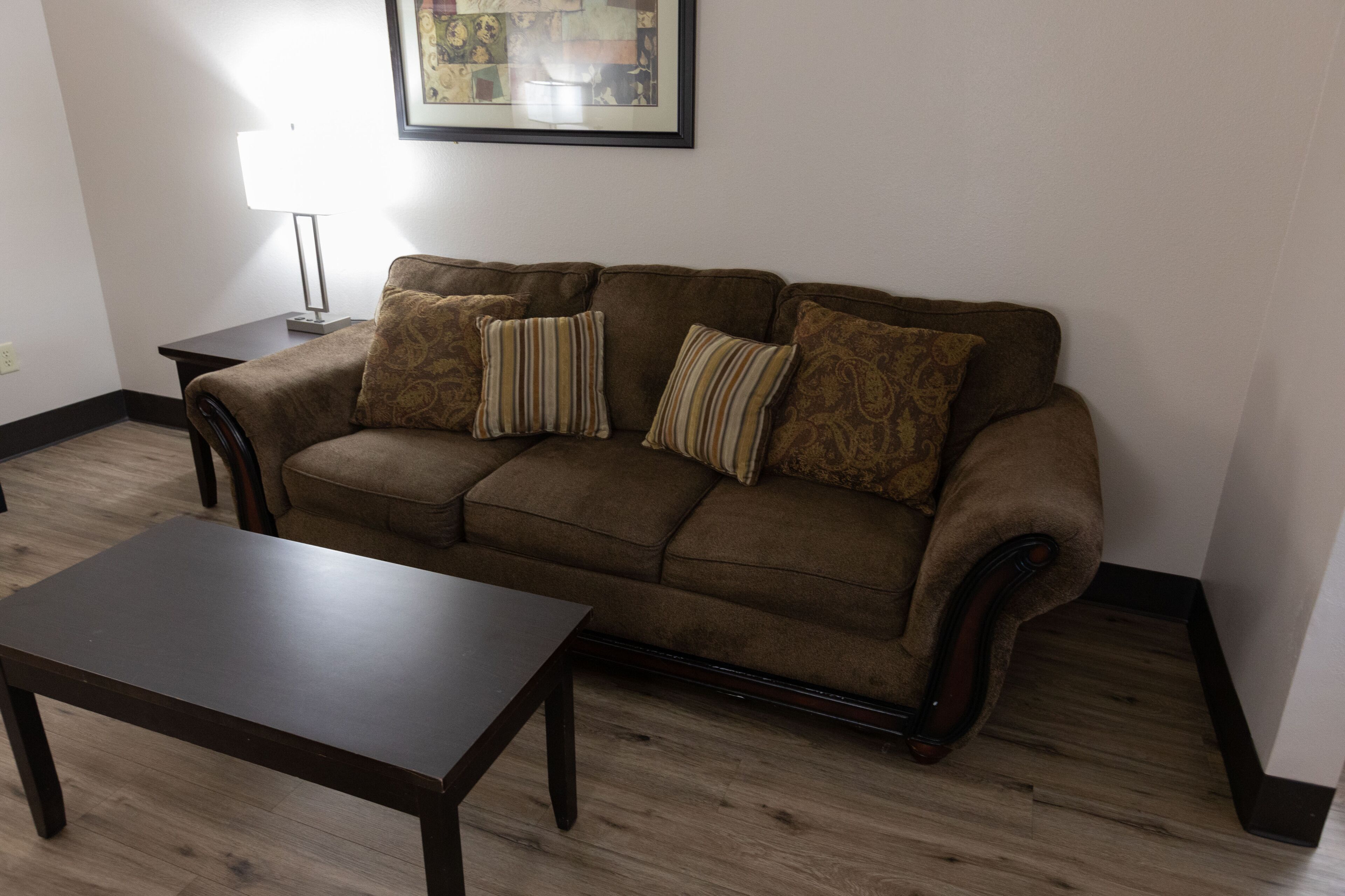 Un salon avec un canapé marron, deux coussins à rayures, une table basse en bois et un tableau encadré accroché au mur.