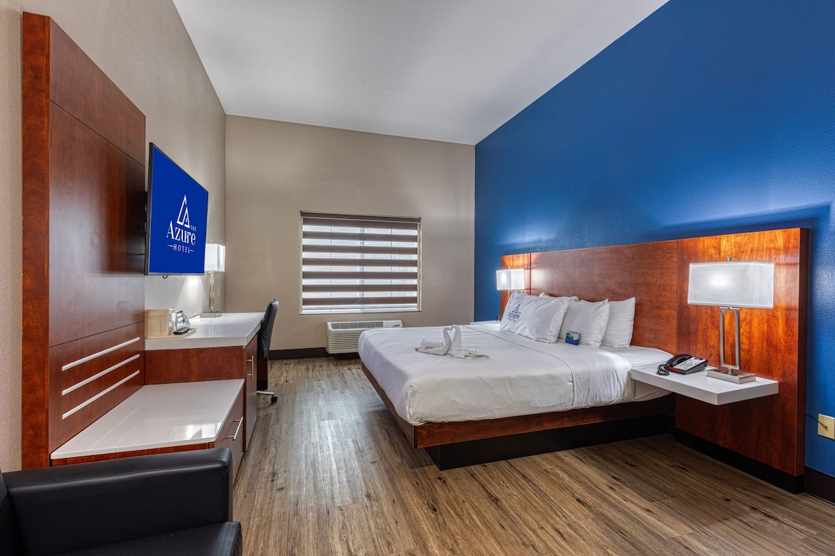 Une chambre d’hôtel équipée d’un lit, d’une table de chevet, d’un bureau, d’une chaise et d’un téléviseur fixé au mur.