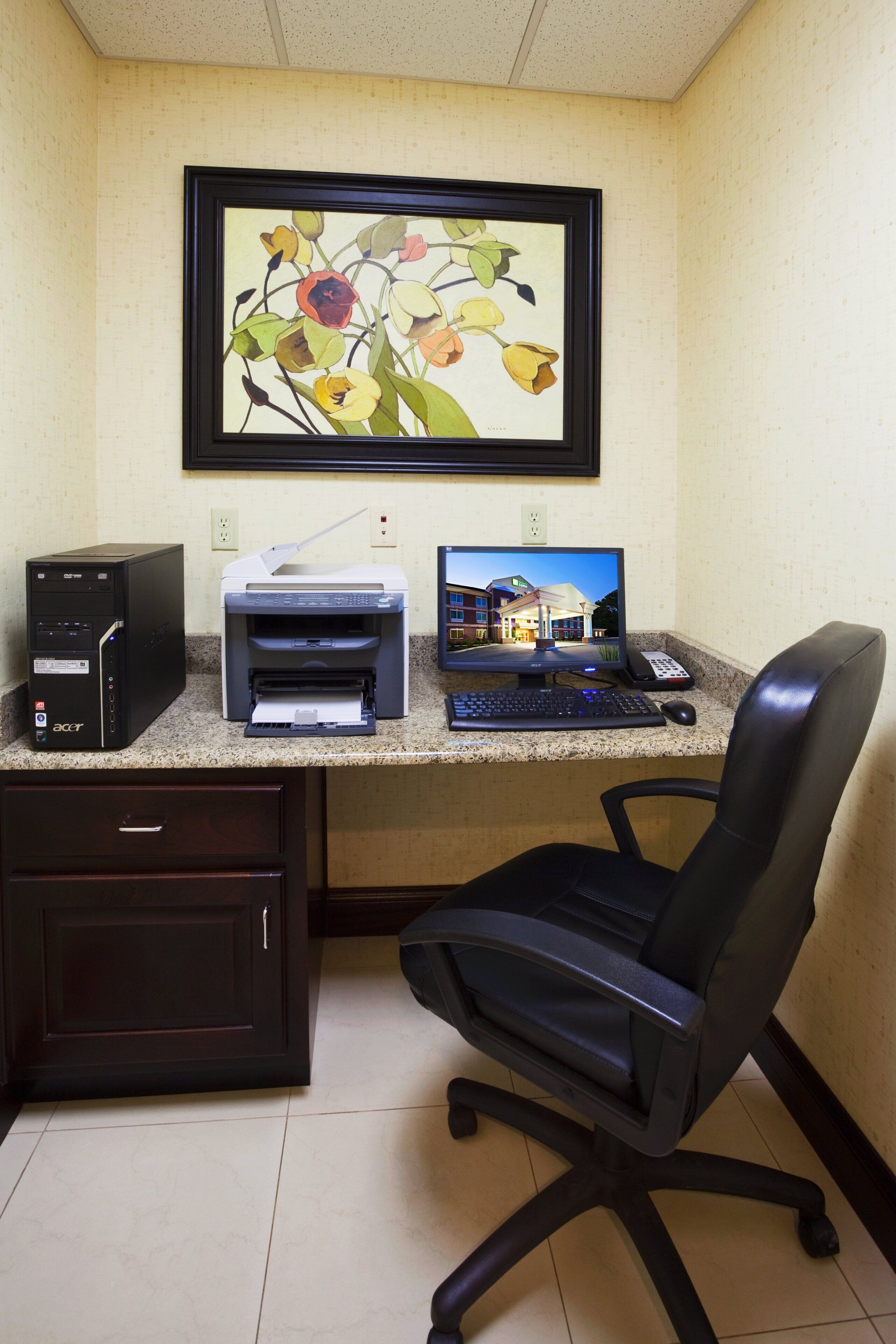 Habitación de hotel con escritorio, impresora, computadora y una obra de arte floral enmarcada en la pared.