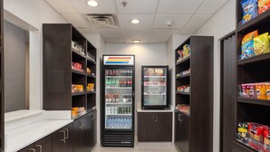 A clean, well-organized snack and beverage area with shelves stocked with various snacks and a refrigerated display case. - Holiday Inn Express & Suites Carrollton by IHG (Carrollton)