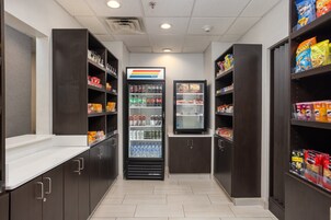 Un área limpia y ordenada para aperitivos y bebidas, con estantes llenos de diferentes opciones y un refrigerador con productos frescos.