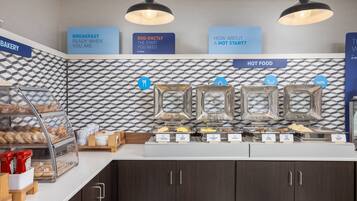 A breakfast buffet area with labeled food stations, including options for eggs, cheese, and sausages.