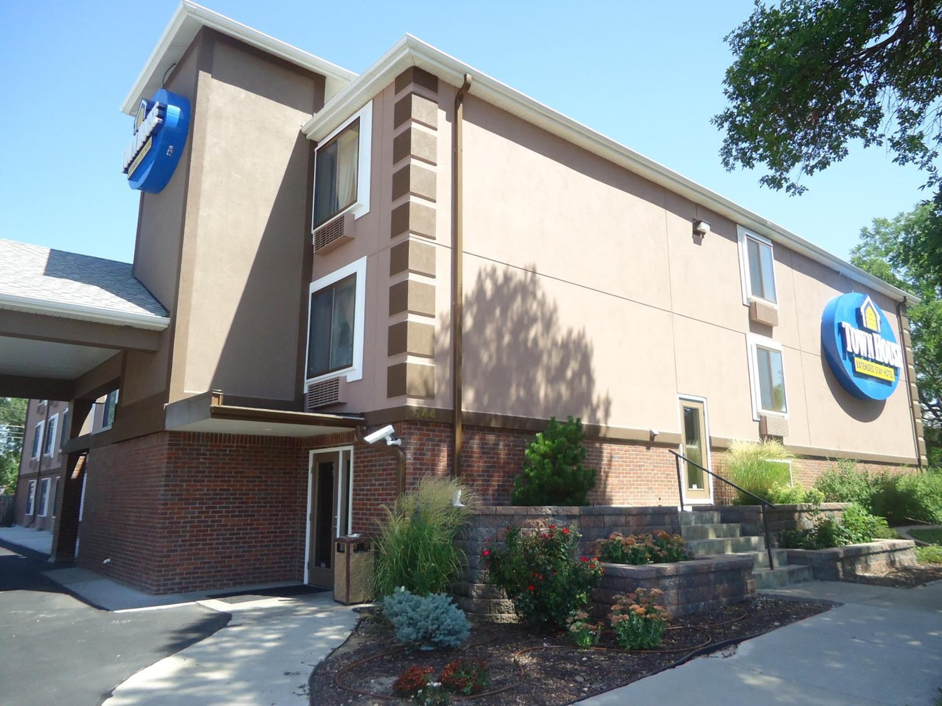 Un Town House Extended Stay Hotel con facciata in mattoni, un grande cartello blu e un'area d'ingresso curata.